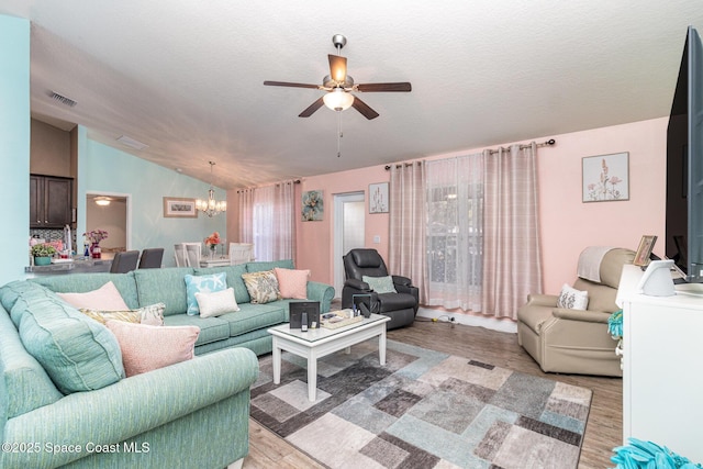 living room featuring ceiling fan with notable chandelier, lofted ceiling, a textured ceiling, and light hardwood / wood-style flooring