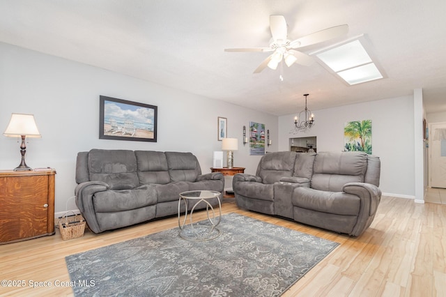 living room featuring hardwood / wood-style floors, ceiling fan with notable chandelier, and a skylight