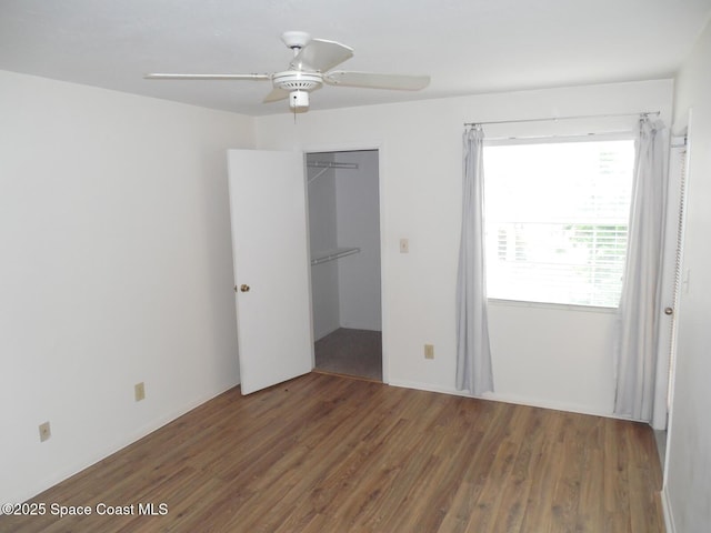 unfurnished bedroom with ceiling fan, a closet, a spacious closet, and dark hardwood / wood-style floors