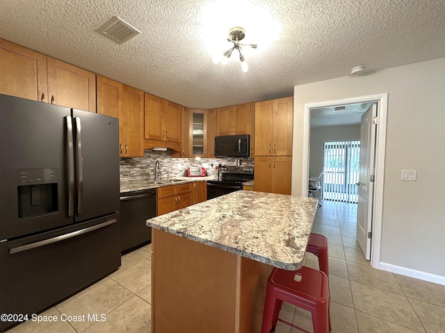 kitchen featuring a kitchen island, black appliances, sink, light stone countertops, and a kitchen breakfast bar