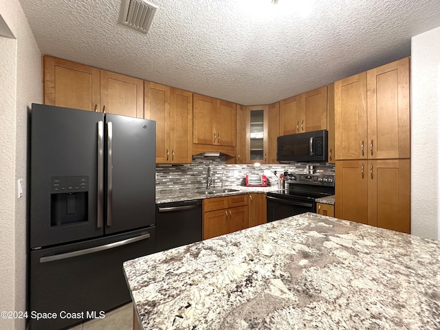 kitchen featuring decorative backsplash, a textured ceiling, black appliances, light stone counters, and sink