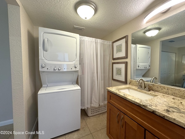 laundry area featuring stacked washer and dryer, light tile patterned floors, a textured ceiling, and sink