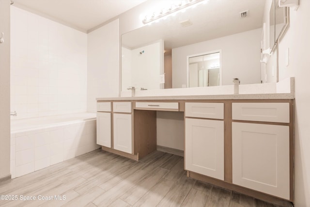 bathroom featuring vanity, wood-type flooring, and a relaxing tiled tub