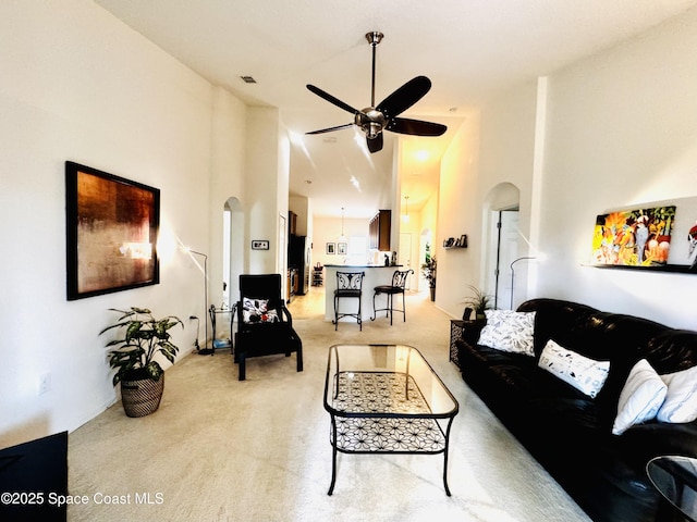 carpeted living room with ceiling fan and a high ceiling