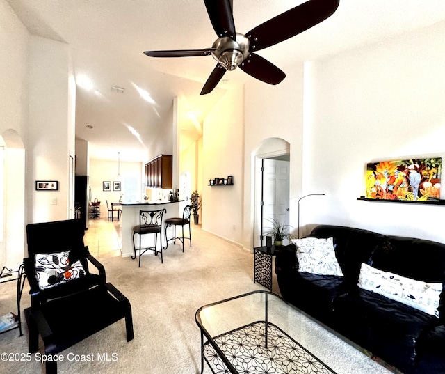 carpeted living room with ceiling fan and high vaulted ceiling