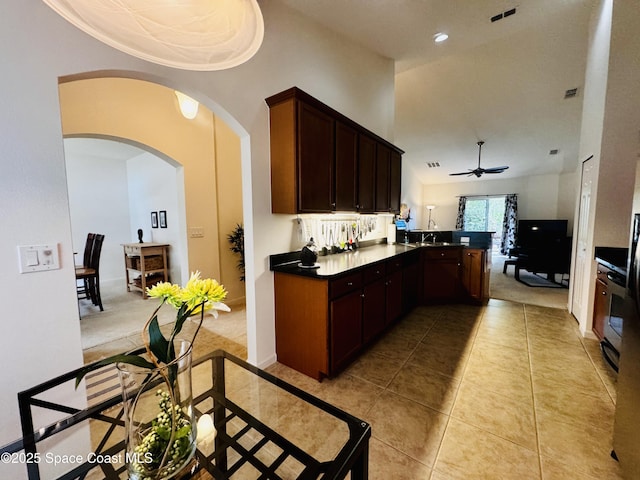 kitchen with kitchen peninsula, dark brown cabinetry, ceiling fan, light tile patterned floors, and a high ceiling