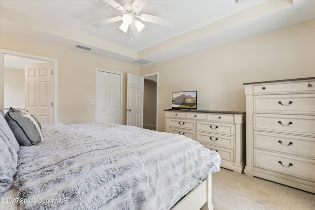 bedroom with light carpet, a tray ceiling, and ceiling fan