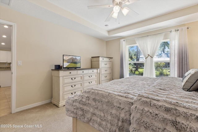 bedroom with ceiling fan, a raised ceiling, and light carpet