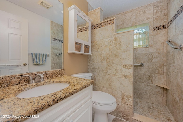 bathroom with tiled shower, vanity, and toilet