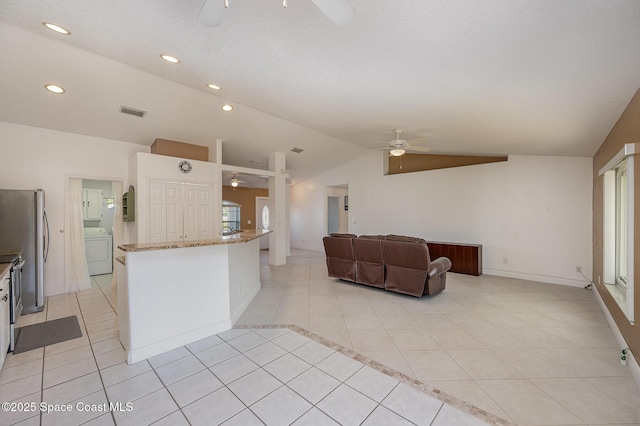 kitchen featuring light stone counters, washer / clothes dryer, stainless steel fridge, lofted ceiling, and light tile patterned flooring