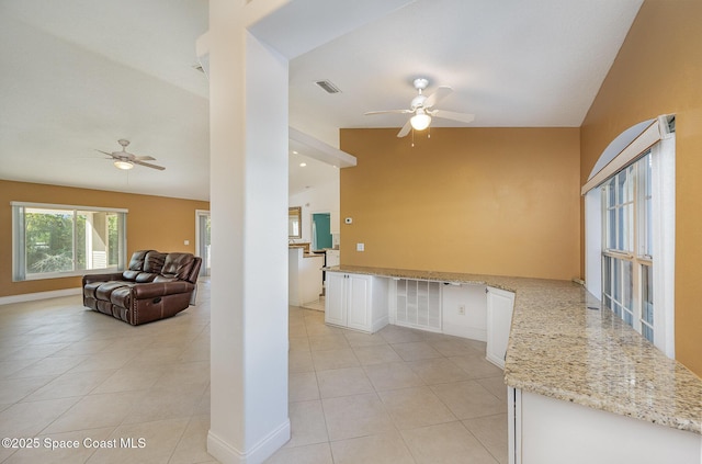 kitchen featuring light stone countertops, white cabinets, light tile patterned flooring, and vaulted ceiling