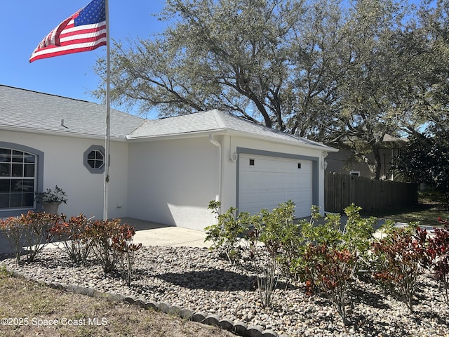 view of side of home featuring roof with shingles, an attached garage, fence, and stucco siding