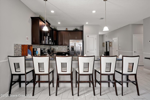 kitchen featuring pendant lighting, backsplash, a breakfast bar area, dark brown cabinetry, and stainless steel appliances