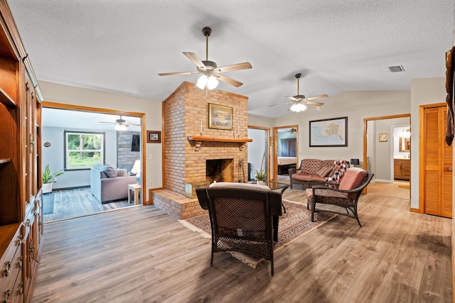 living room featuring a fireplace, light hardwood / wood-style floors, vaulted ceiling, and ceiling fan