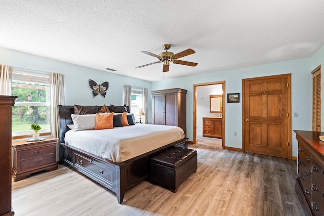 bedroom with ensuite bath, ceiling fan, multiple windows, and light wood-type flooring