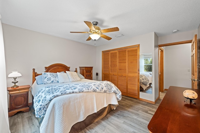 bedroom with a textured ceiling, a closet, light hardwood / wood-style flooring, and ceiling fan