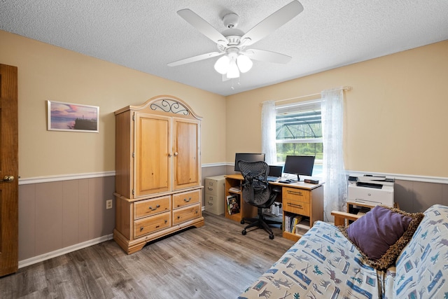 home office featuring ceiling fan, wood walls, light hardwood / wood-style floors, and a textured ceiling