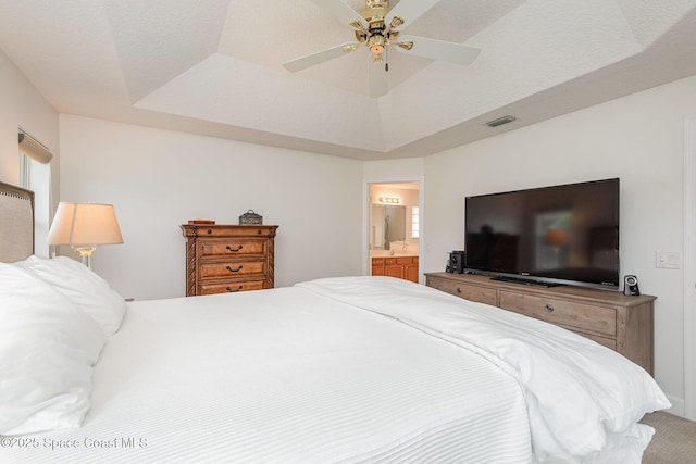 bedroom featuring a raised ceiling, connected bathroom, ceiling fan, and carpet