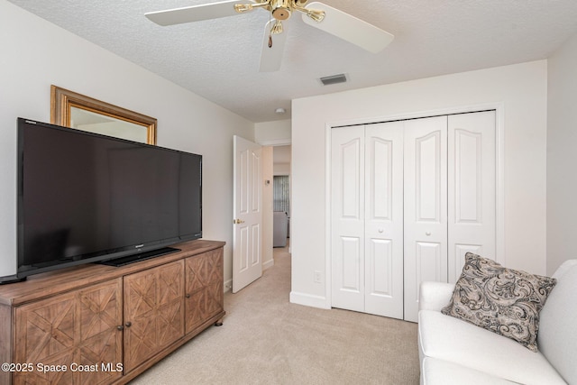 living area with light carpet, ceiling fan, and a textured ceiling