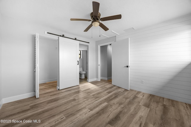 unfurnished bedroom featuring hardwood / wood-style floors, ensuite bath, ceiling fan, and a barn door