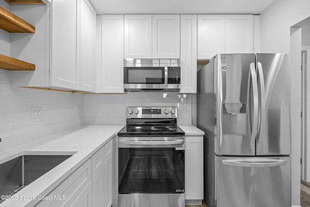 kitchen with backsplash, light stone counters, stainless steel appliances, sink, and white cabinets