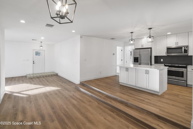 kitchen with backsplash, stainless steel appliances, pendant lighting, white cabinets, and a center island