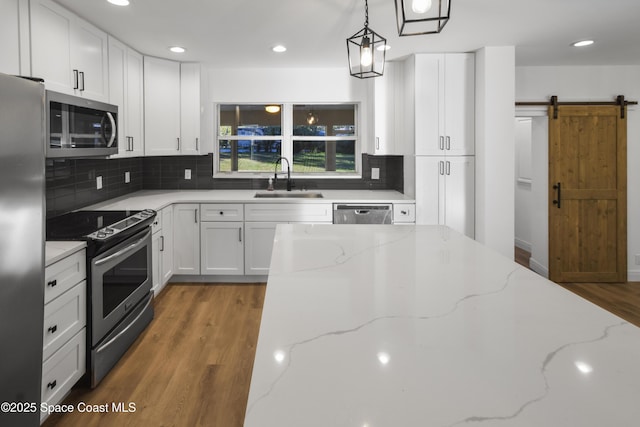 kitchen featuring appliances with stainless steel finishes, light stone counters, sink, a barn door, and white cabinetry