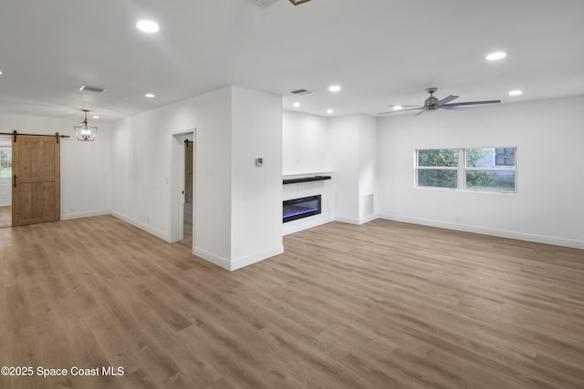 unfurnished living room featuring a barn door, light hardwood / wood-style floors, and ceiling fan