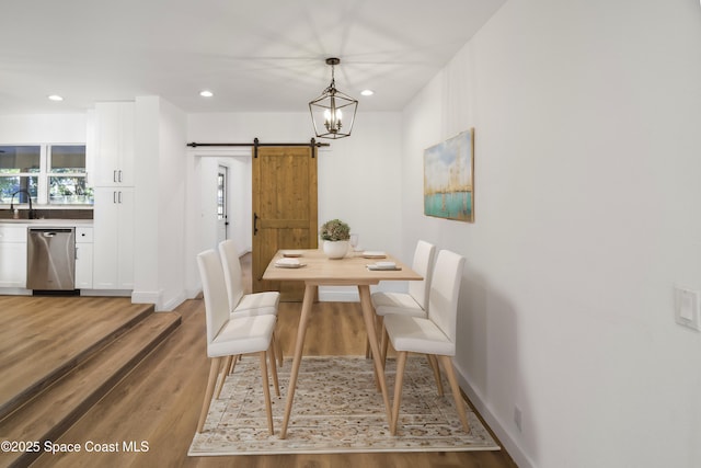 dining room with a barn door, sink, wood-type flooring, and an inviting chandelier