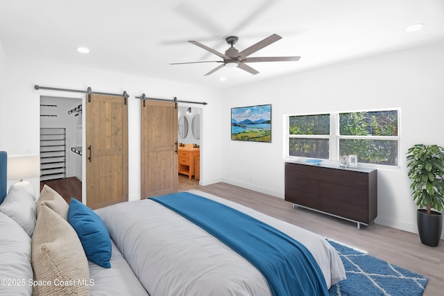 bedroom with a barn door, light hardwood / wood-style flooring, ceiling fan, and connected bathroom