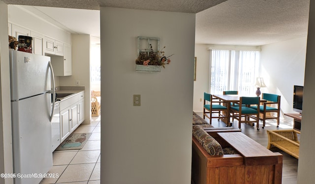 kitchen with a textured ceiling, white cabinets, white fridge, and light tile patterned floors