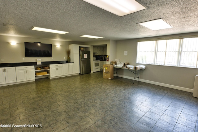 interior space with white range with electric stovetop, stainless steel refrigerator, and white cabinets