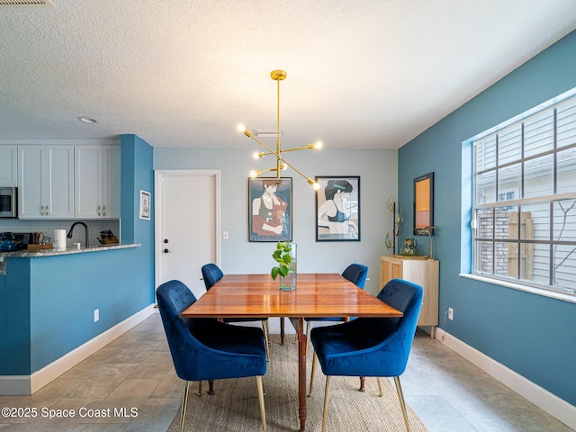 dining area featuring sink, a textured ceiling, and an inviting chandelier