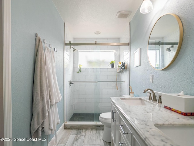 bathroom featuring vanity, a shower with shower door, a textured ceiling, and toilet