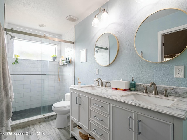 bathroom with a textured ceiling, vanity, toilet, and walk in shower