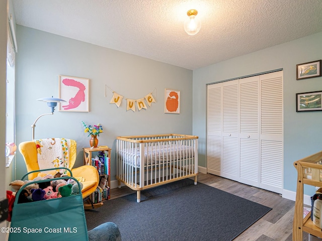 bedroom with hardwood / wood-style floors, a closet, a textured ceiling, and a nursery area