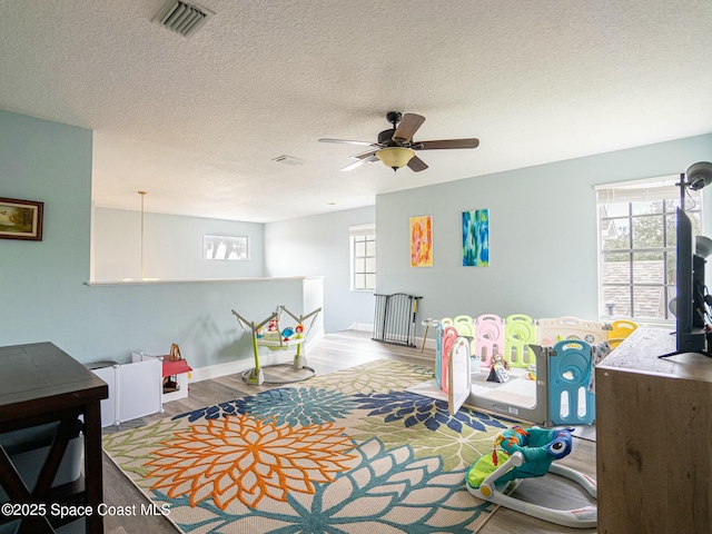 rec room featuring ceiling fan, light hardwood / wood-style floors, plenty of natural light, and a textured ceiling