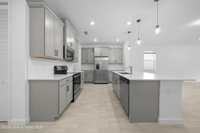 kitchen featuring decorative light fixtures, appliances with stainless steel finishes, a kitchen island with sink, and tasteful backsplash