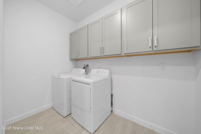 clothes washing area with cabinets, light hardwood / wood-style flooring, and washing machine and clothes dryer