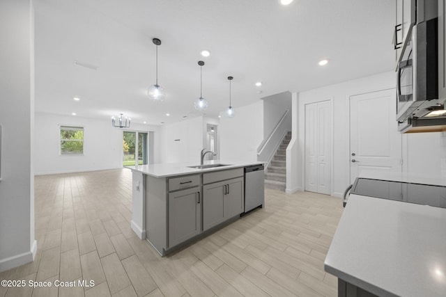 kitchen with appliances with stainless steel finishes, decorative light fixtures, sink, gray cabinets, and a center island with sink