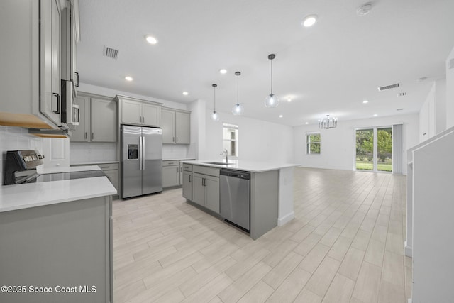 kitchen featuring pendant lighting, appliances with stainless steel finishes, sink, gray cabinets, and a center island with sink