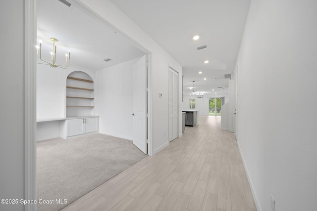 hall with light wood-type flooring and a chandelier