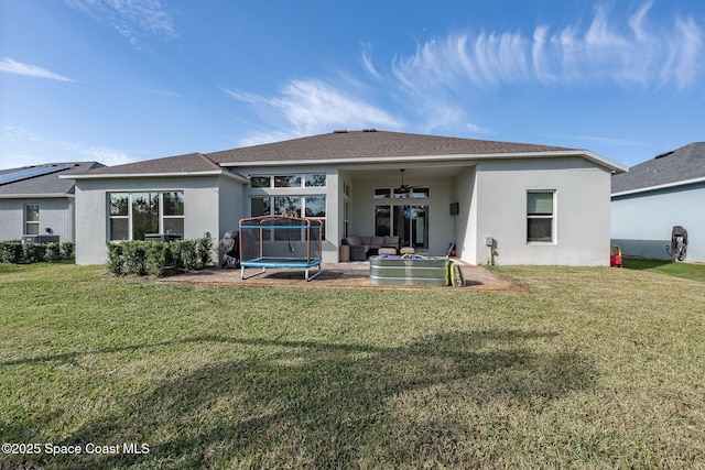 rear view of house with a lawn, ceiling fan, an outdoor living space, and a trampoline