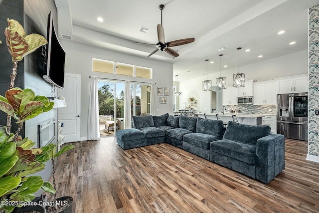 living room with a raised ceiling, ceiling fan, dark hardwood / wood-style flooring, and a high ceiling