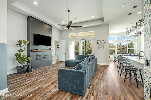 living room featuring a fireplace, a high ceiling, ceiling fan, and dark wood-type flooring