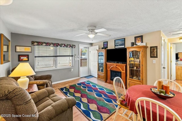 living room featuring ceiling fan, light hardwood / wood-style flooring, and a textured ceiling