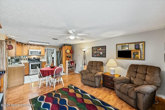 living room with a textured ceiling, light hardwood / wood-style flooring, ceiling fan, and sink