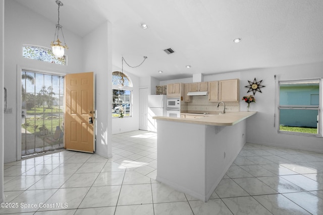 kitchen with kitchen peninsula, backsplash, white microwave, light brown cabinets, and decorative light fixtures