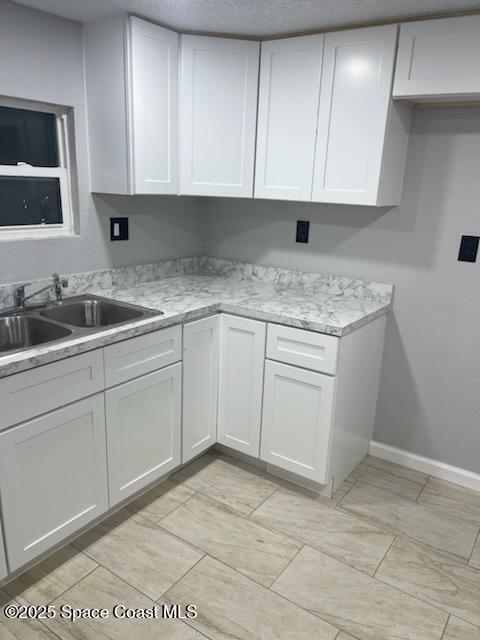 kitchen featuring white cabinets, light stone counters, and sink