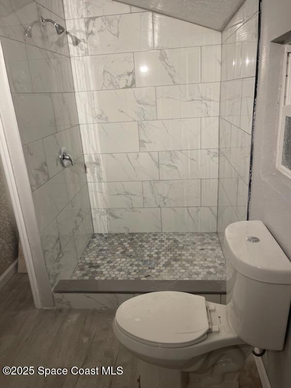 bathroom featuring a tile shower, hardwood / wood-style floors, and toilet